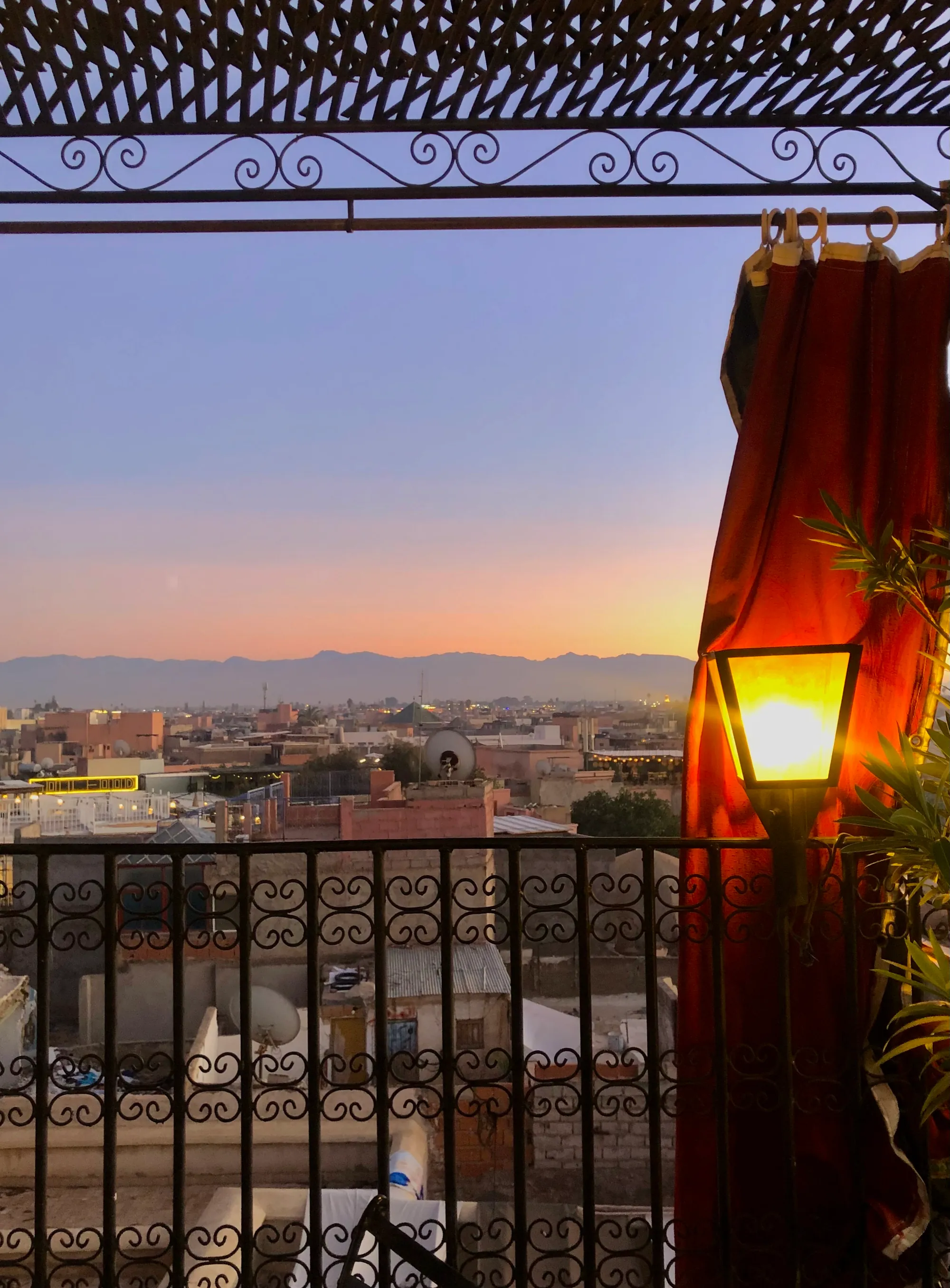 Sunset from the terrace: the medina, the line of the Atlas on the horizon and a lit lantern under the pergola