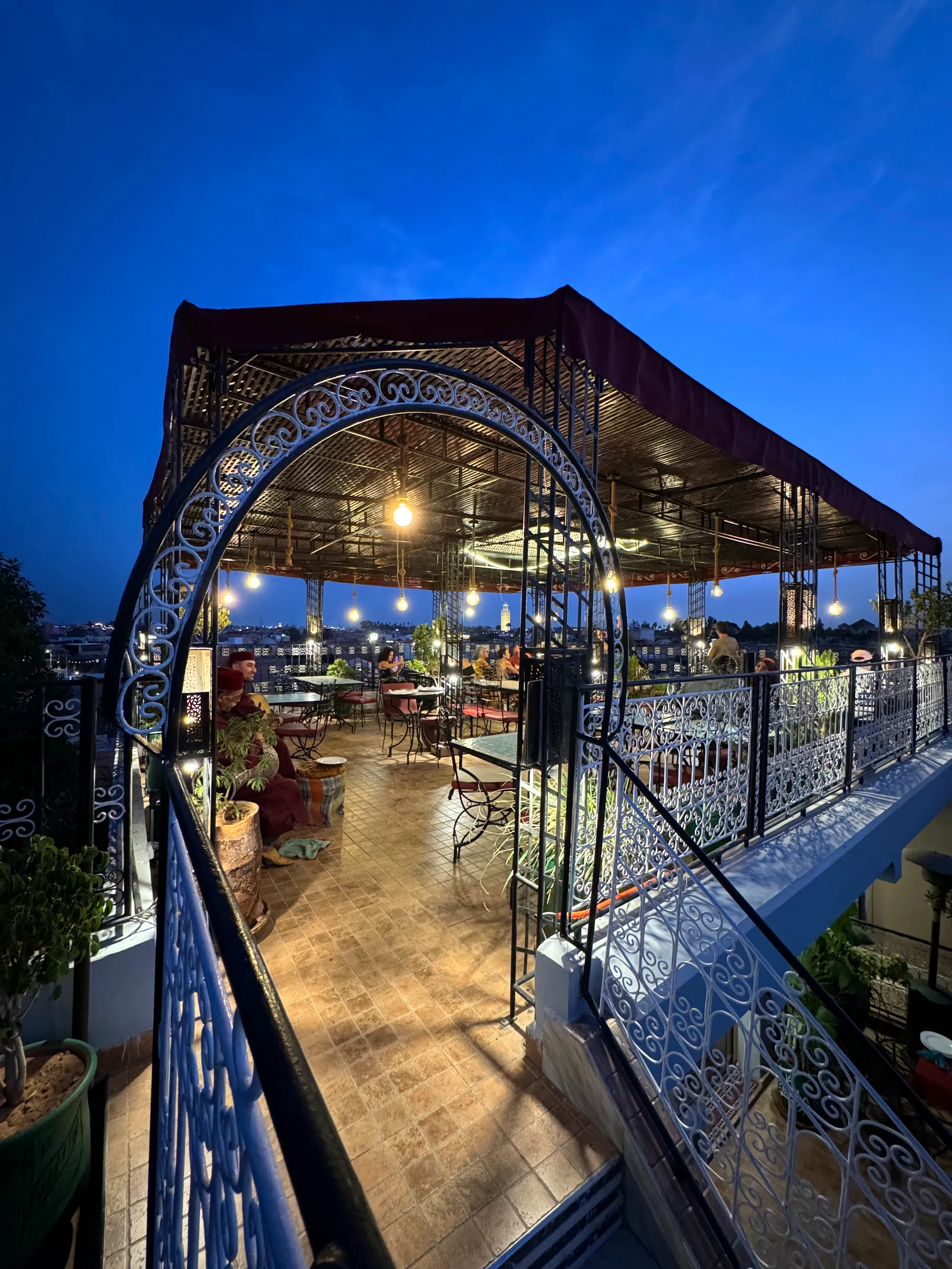 The terrace after dark: strung bulbs under the iron pergola and the lit medina behind