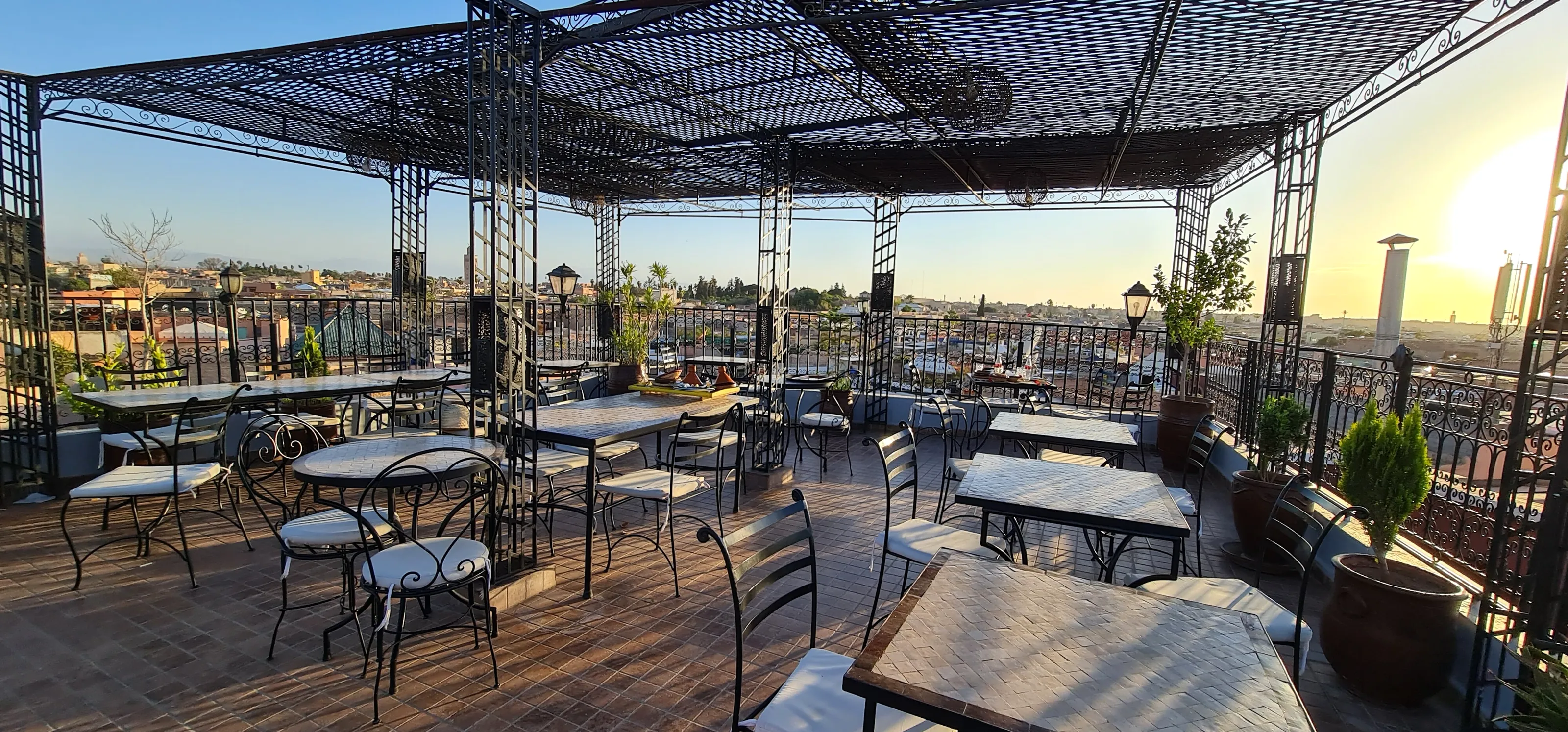 The row of tables against the terrace railing, low sun over the medina rooftops